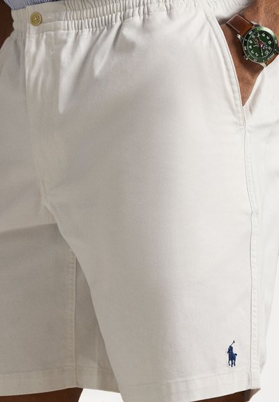 Shorts en coton blanc avec une taille élastique, dotés d'un logo bleu brodé et de poches latérales. Texture lisse et coupe décontractée.