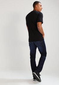 Czarny t-shirt z krótkim rękawem zestawiony z ciemnoniebieskimi dżinsami. Stylizacja uzupełniona czarnymi trampkami z teksturowaną podeszwą.