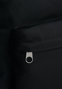 Svart tyg med en slät textur, utrustat med en ficka med dragkedja och en cirkulär silverfärgad dragflik samt sydda detaljer längs kanterna.