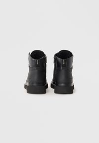 Botine negre până la gleznă, cu un superior din piele netedă, guler căptușit, fermoare laterale și o talpă din cauciuc masivă. Prezintă accente de cusătură albă.