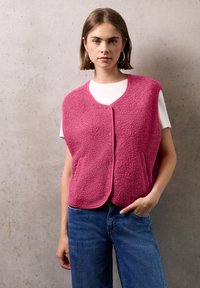 Fleecev�äst i stark rosa med rund hals, framknappar och sidofickor, lagd över en vit t-shirt och ihop med blå jeans.