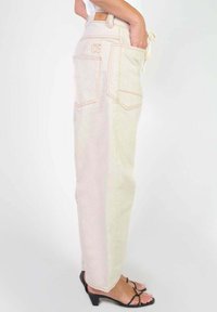 Pantalons taille haute beige clair avec des coutures orange, deux poches arrière et une coupe droite. Le matériau semble doux avec une texture lisse.