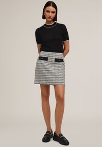 Haut tricot noir à manches courtes et bord blanc, associé à une mini-jupe rayée gris et noir avec poches avant et accents dorés.