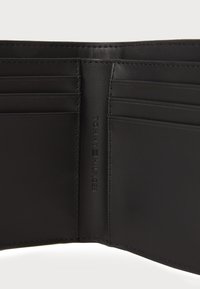 Zwarte leren portemonnee interieur met meerdere kaartsleuven, reliëf "TOMMY HILFIGER" logo, gladde textuur en nette stiksels.