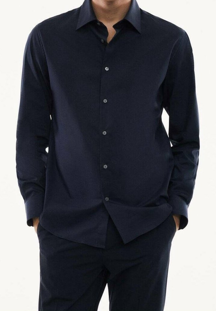 Chemise bleu marine à manches longues avec boutons, fabriquée en tissu lisse, avec un col pointu et des détails subtils de boutons sur le devant.