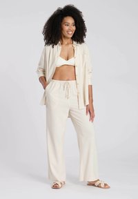 Chemise en lin beige avec des boutons dorés, accompagnée d'un pantalon léger à cordon de serrage assorti. Design simple, texture respirante et coupe ample.
