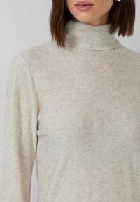Sweter w kolorze jasnego beżu z golfem, wykonany z miękkiej dzianiny; charakteryzuje się subtelnym połyskiem z małymi srebrnymi drobinkami w całym materiale.