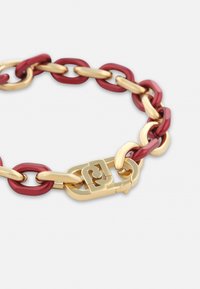 Punane ja kuldne kett käevõru, millel on vahelduvad läikivad lingid ning turvaline kuldne lukustus koos logo detailiga. Ühtlane pind kogu ulatuses.