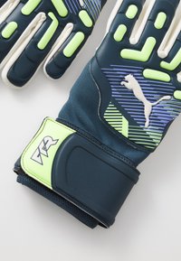 Gepolsterte Torwarthandschuhe mit marineblauen und grünen Akzenten, strukturiertem Grip, elastischem Handgelenkband und Logodetails am Bund.