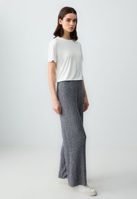 Witte T-shirt met korte mouwen gecombineerd met grijze geribbelde wijde broek, met een gestructureerde stof en een ontspannen silhouet, afgewerkt met witte sneakers.