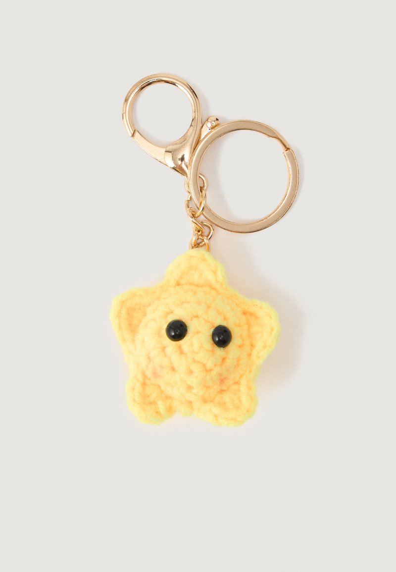 Yellow crocheted star with black eyes attached to gold keychain ring and clasp on white background.