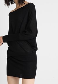 Svart stickad tröja med en off-shoulder-design. Långa ärmar, lös passform, lagrad över en figurnära svart ribbad kjol. Strukturerad tyg.