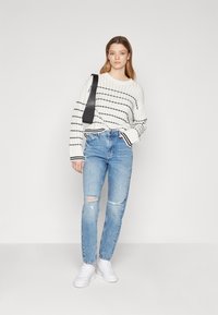 Vit stickad tröja med svarta ränder, i kombination med ljusblå slitna jeans och vita sneakers, kompletterad med en svart axelväska.