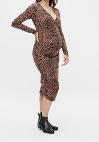 Maternity dress in brown with black abstract print. Long sleeves, deep V-neck, and ruching detail at the waist. Paired with black ankle boots.