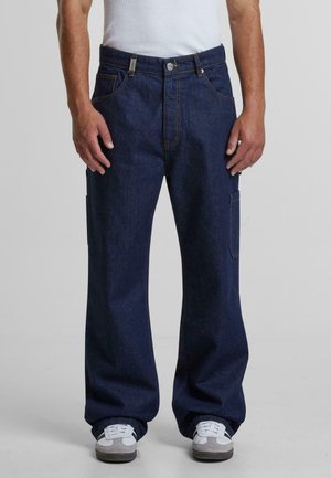 Pantalons cargo en denim bleu foncé avec une coupe décontractée, dotés de coutures orange, de poches latérales et d'une fermeture à bouton. Texture lisse.