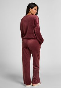 Bordeaux velours loungewear set met een losse lange mouw top en bijpassende broeken met rechte pijpen, van achteren getoond.