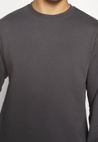 Dark gray long-sleeve t-shirt featuring a crew neckline, smooth texture, and ribbed cuffs. Simple, clean design without patterns or accents.