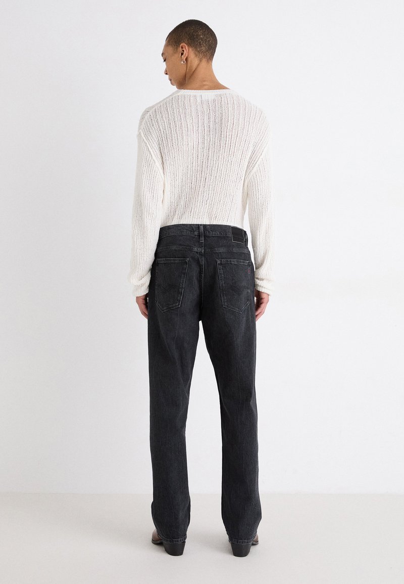 Weißer Strickpullover mit gerippter Textur, kombiniert mit schwarzen Denim-Jeans in klassischer Passform. Glatte Oberfläche, minimalistisches Design, keine sichtbaren Muster.