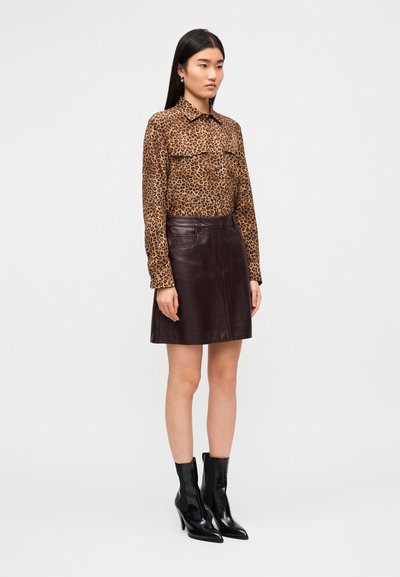 Πουκάμισο με λεοπάρ σχέδιο και κουμπιά, δύο τσέπες στο στήθος· καφέ δερμάτινη μίνι φούστα με λεία υφή· μαύρα μποτάκια αστραγάλου με τακούνι και μυτερά δάχτυλα.
