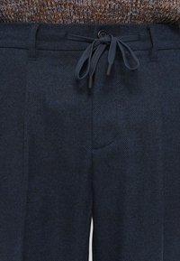 Navy textured trousers featuring a drawstring waist, side pockets, and a subtle woven pattern. Material appears soft and breathable.