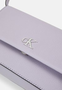 Fialová kožená kabelka s texturovaným povrchem, na klopě se stříbrným logem "CK" a kontrastním černým prošitím podél okrajů.