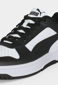 Ασπρόμαυρο αθλητικό Puma με κορδόνια, υφασμένο δέρμα και λογότυπο Puma στη γλώσσα, εμφανίζεται από πλάγια γωνία.
