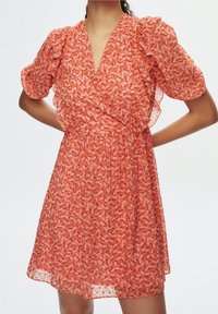 Abito con motivo floreale in tonalità di arancione e rosa, realizzato in tessuto leggero. Caratterizzato da scollo a V, maniche corte a sbuffo e vita arricciata.