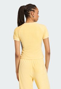 Žltý velúrový top s krátkym rukávom a priliehavým strihom, s raglánovými rukávmi, so soft textúrou a bezšvovým lemom v oblasti pása.