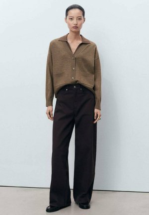 Cárdigan de punto marrón con cuello y botones, acompañado de pantalones oscuros de tiro alto y pierna ancha. Diseño simple, colores neutros, textura suave.