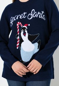 Granatowy sweter z napisem "Sekretny Mikołaj", przedstawiający uśmiechniętego pingwina w czapce Mikołaja, trzymającego laskę cukrową.