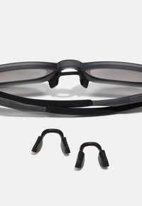 Czarnie okulary przeciwsłoneczne o eleganckim designie, elastycznych ramionach i szarych soczewkach. Zawierają wymienne czarne noski.