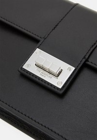 Borsa a tracolla in pelle nera con chiusura a patta, dotata di una fibbia metallica con tre pulsanti e marchio impresso. Bordature cucite con cura.