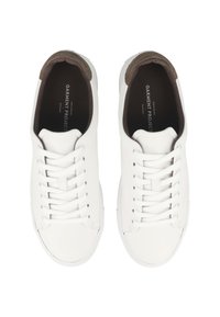Un paio di sneakers bianche basse con lacci bianchi e colli imbottiti marroni, viste dall'alto su uno sfondo bianco.