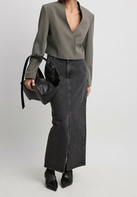 Blazer verde oliva a forma accorciata con scollatura a V profonda, abbinato a una gonna di jeans nera a vita alta con uno spacco frontale e tacchi a punta neri.