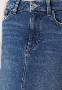 Denim krilo v temno modri barvi z gladko teksturo, vidnimi šivi, zapiranjem na gumb in stranskimi žepi.