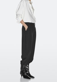 Black tailored trousers with side pockets, paired with a white button-up shirt. Footwear features glossy black, pointed toe ankle boots.