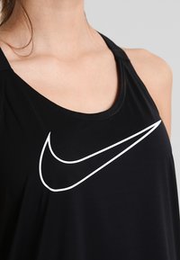 Top sportivo nero realizzato in tessuto liscio con un logo Nike bianco sul petto e design a schiena scoperta.