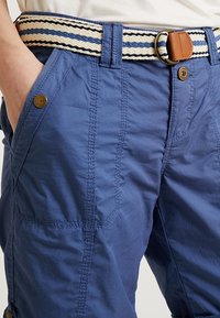 Pantaloncini cargo blu con tessuto strutturato, dotati di tasche laterali, chiusura frontale con bottoni e cintura intrecciata a righe beige e blu.