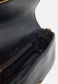 Sac à main en cuir noir avec une texture lisse, doté d'une poche zippée dorée et de détails de couture, mettant en valeur un design intérieur ouvert.