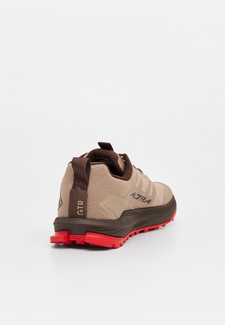 Zapatilla de correr marrón claro con parte superior suave, acentos marrón oscuro, suela roja y talón texturizado, con la marca "ALTRA" en el costado.