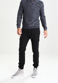 Pull tricot texturé bleu marine, pantalon cargo noir avec poignets élastiques, et baskets grises avec lacets blancs ; tenue décontractée avec poches fonctionnelles.