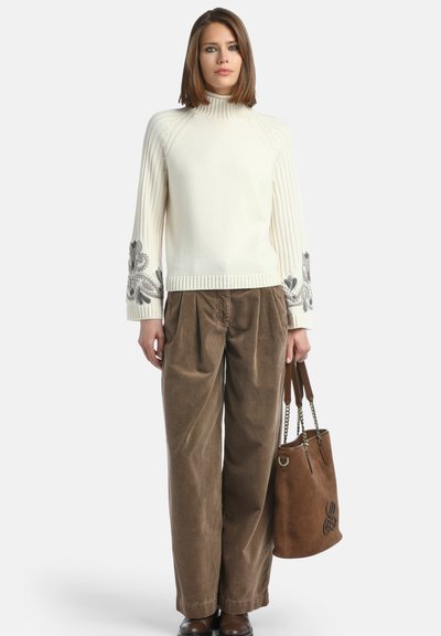 Maglione lavorato a maglia crema con maniche a coste e ricamo floreale, abbinato a pantaloni larghi in velluto a coste marroni e una borsa a tracolla in suede marrone.