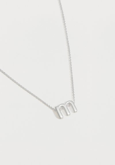 Collier en argent avec pendentif en forme de lettre minuscule « m » sur une fine chaîne, présenté sur fond blanc.