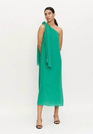 Vestido verde de un solo hombro con una tela fluida y un detalle anudado en el hombro. Largo hasta la mitad de la pantorrilla con una textura suave y ligera.