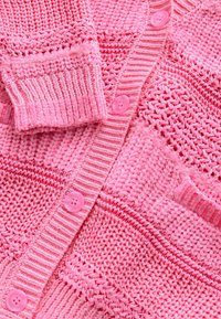Różowy sweter dziewiarski z teksturowanym wzorem, ściągaczami przy mankietach i gładkimi guzikami; wyróżnia się różnorodnymi stylami dzianiny oraz odcieniami różu.