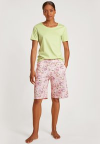 Groene katoenen t-shirt gecombineerd met knielange roze bloemenshorts met een trekkoord in de taille en zakken. Gladde stoftextuur.