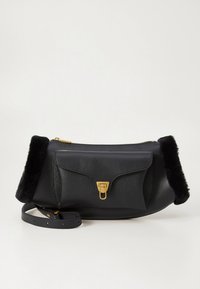 Musta nahkainen olkalaukku, jossa on jämäkkä muoto, pehmeät turkisaksentit sivuilla, kullanväriset metalliosat ja etutasku läpällä.