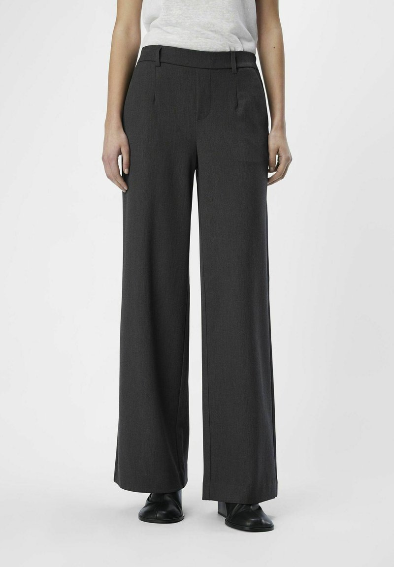 Pantalones de pierna ancha en tela gris oscuro, con una cintura entallada, parte frontal plana y bolsillos laterales. Combinados con calzado negro.
