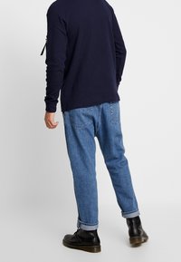 Marinblå långärmad tröja, avslappnade blå denimjeans och svarta ankelboots med texturerad sula, uppvikta fållar på jeansen.