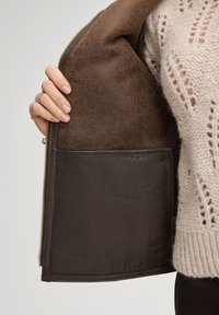 Brązowa skórzana torba o fakturowanej powierzchni, wnętrze wykończone gładką, ciemnobrązową podszewką z kieszenią. Zamek błyskawiczny wzdłuż jednego brzegu.